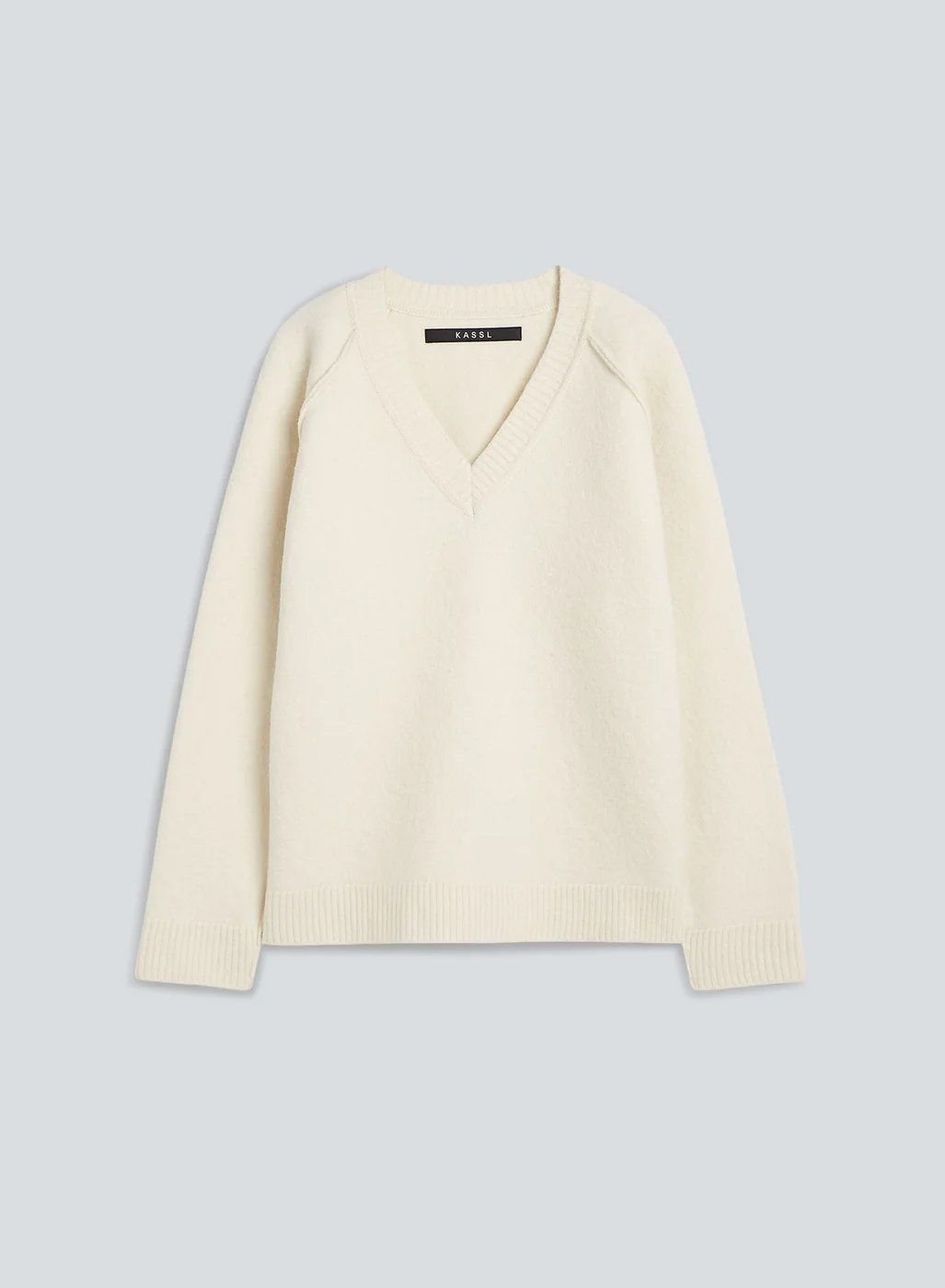 Cream V-neck knit sweater with raglan sleeves, flat lay on pale grey-blue background