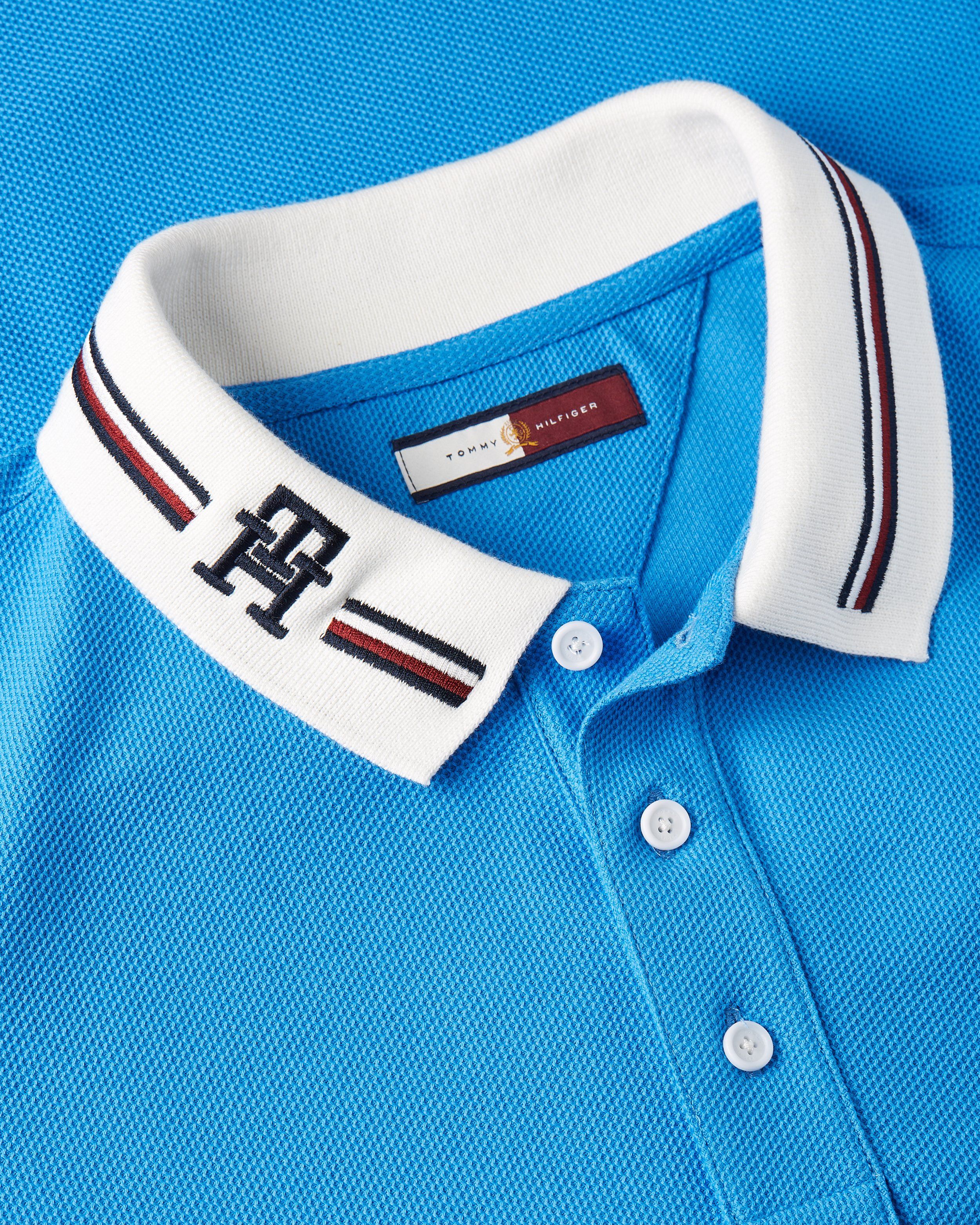 Close-up of bright blue polo with white striped collar and TH monogram, Tommy Hilfiger
