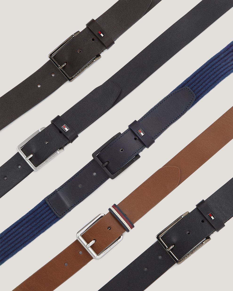Leather and woven belts in black, navy and brown laid diagonally on off-white, Tommy Hilfiger
