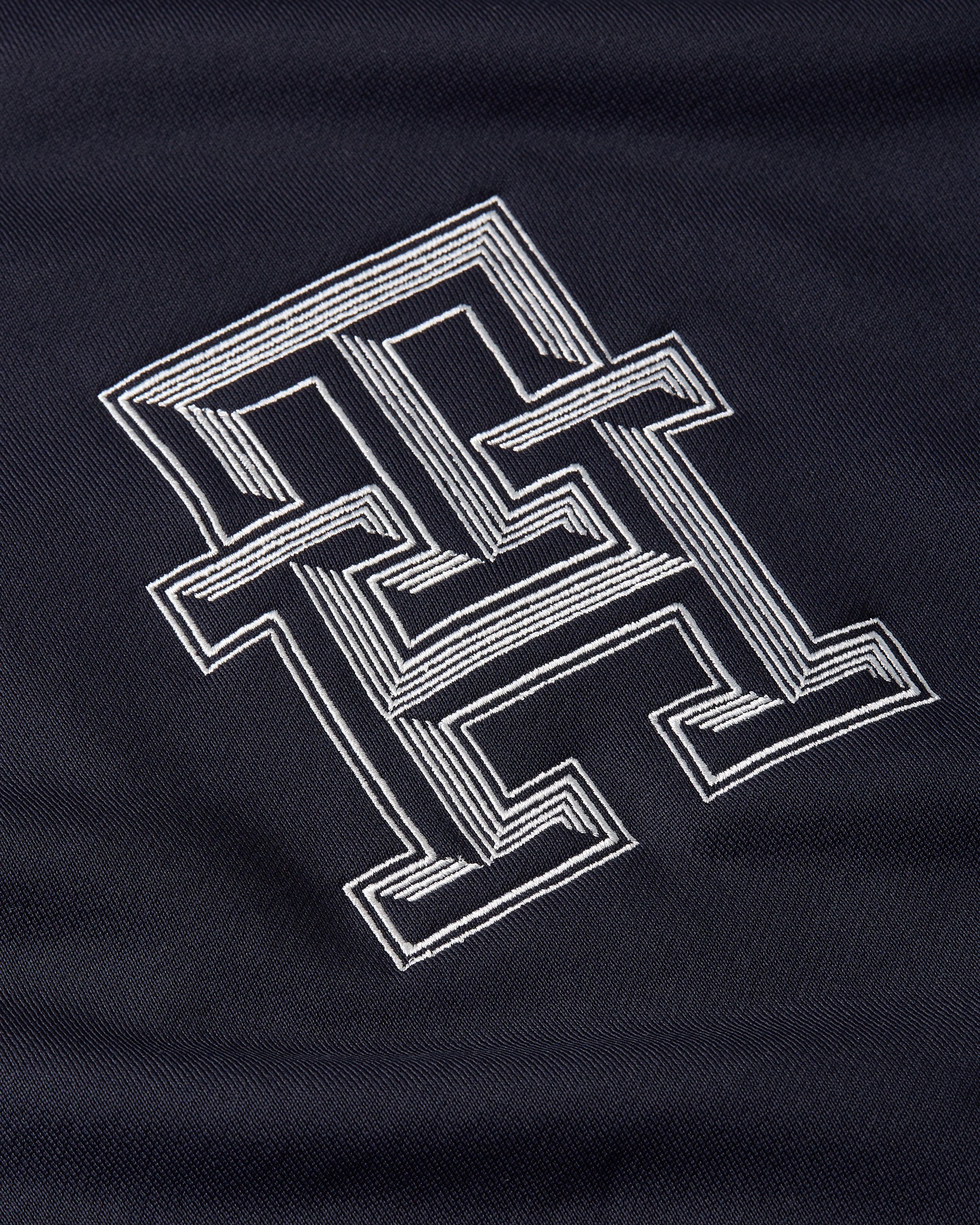 Close-up of an embroidered TH monogram on navy fabric, Tommy Hilfiger