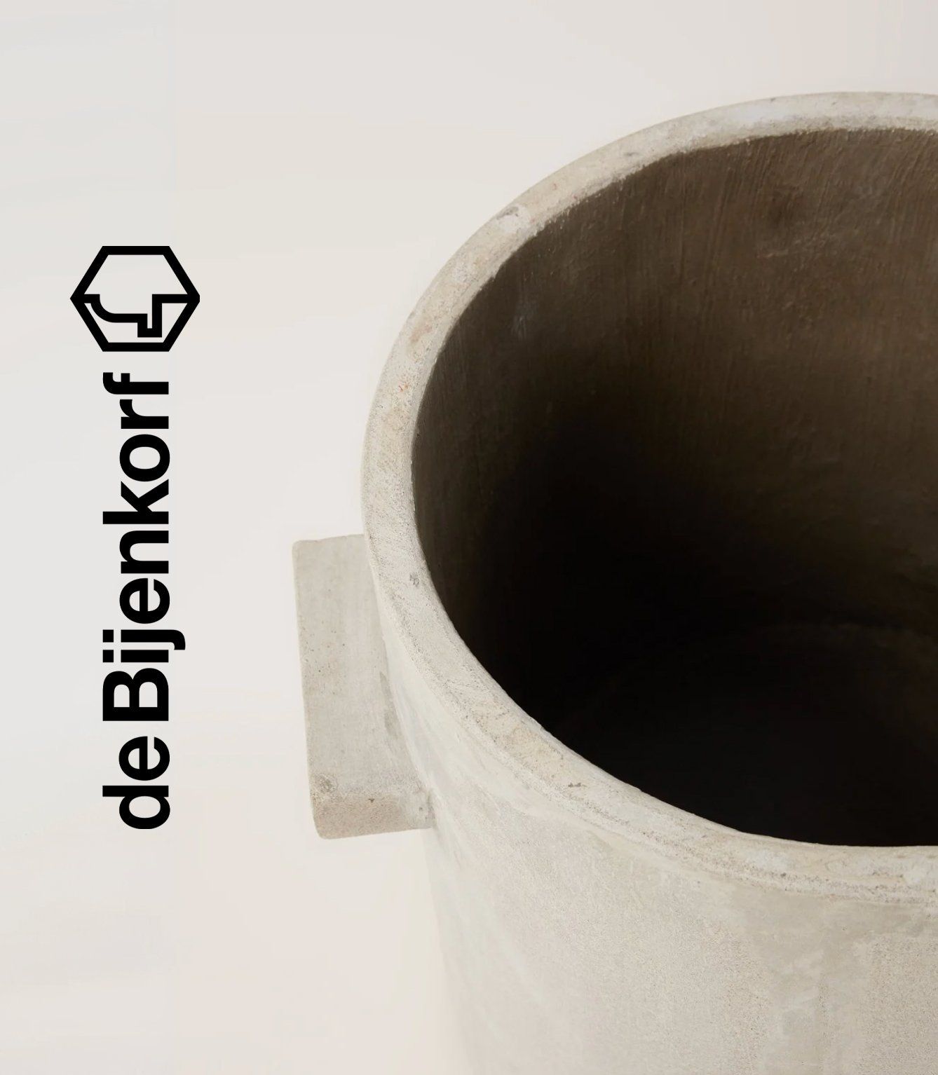 Close-up of a grey concrete planter with side handles on cream background, de Bijenkorf