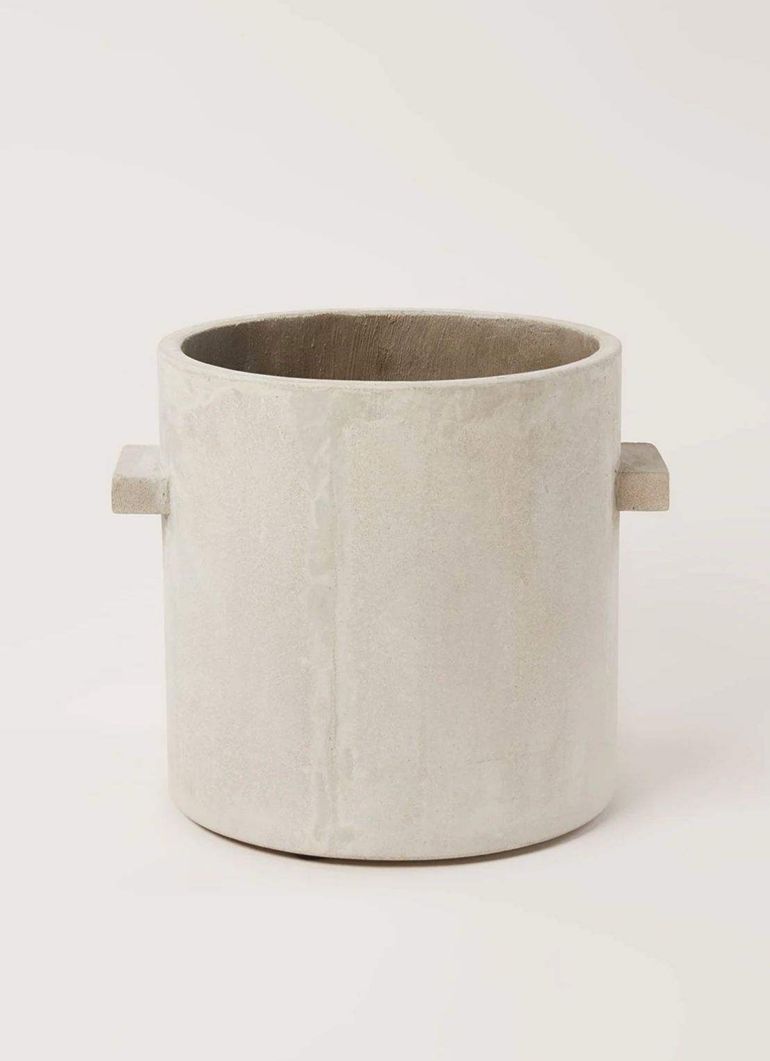 Grey concrete plant pot with two side handles on a warm off-white background, soft daylight