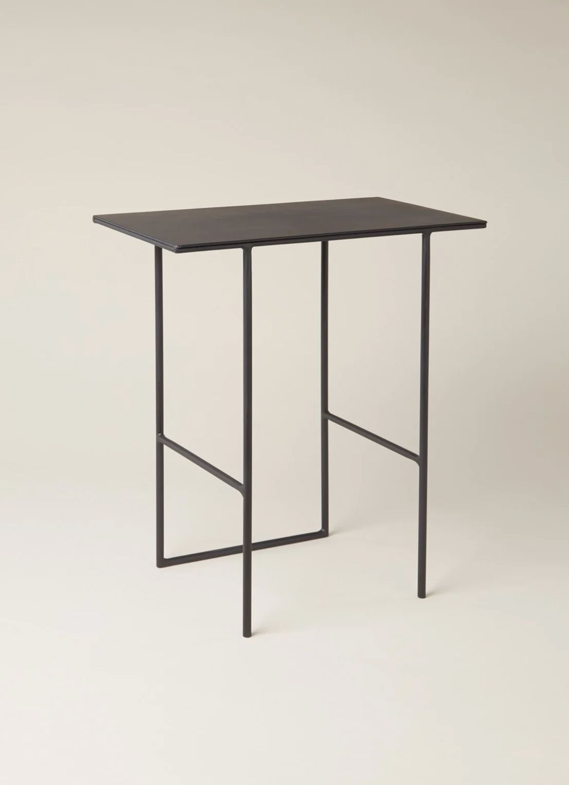 Black metal side table with thin angled legs on a warm neutral background