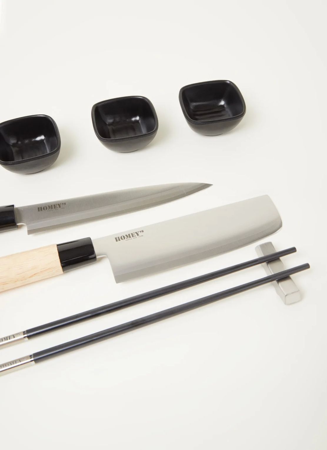 Black sushi dishes, knives and chopsticks with rests arranged on an off-white surface, cropped table top shot