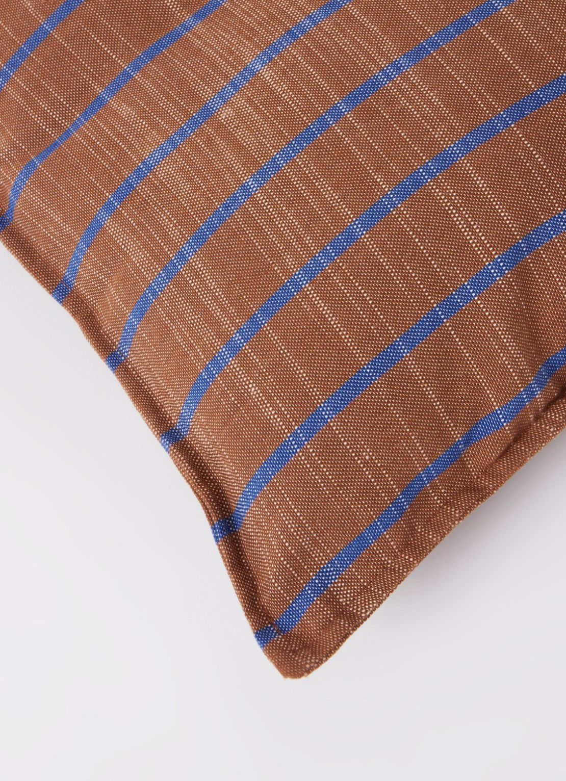Close-up of brown linen cushion corner with blue stripes and piped edge on white background