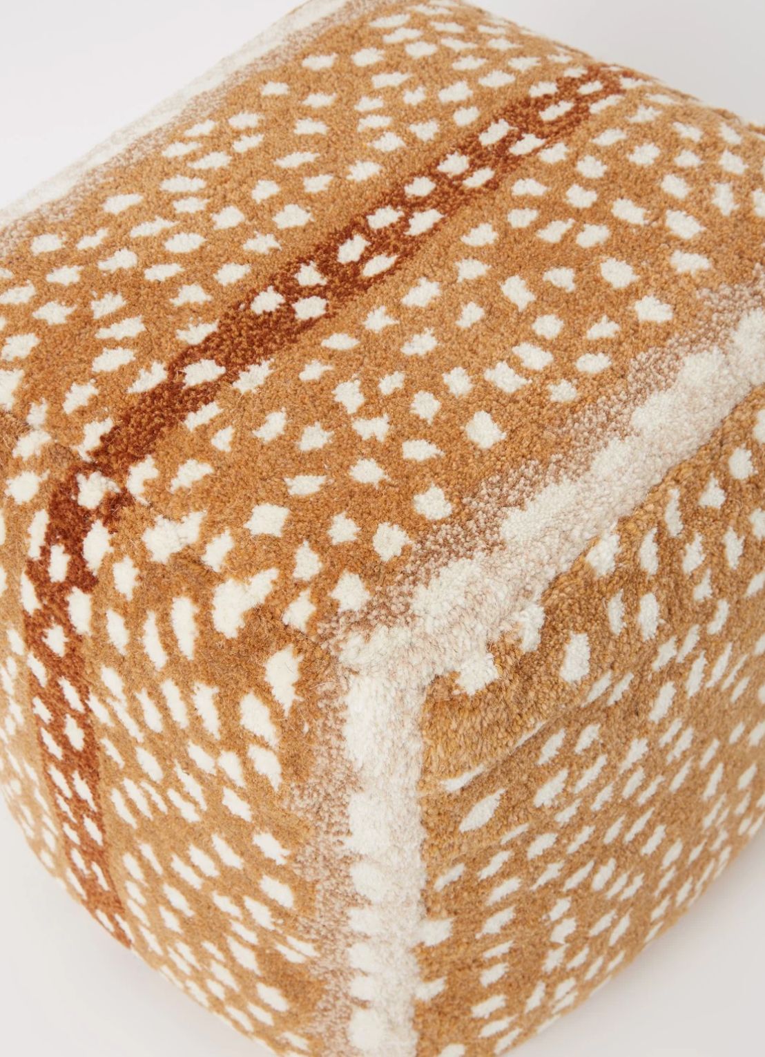 Close-up of a spotted tan and cream pouf showing tufted texture and a brown stripe
