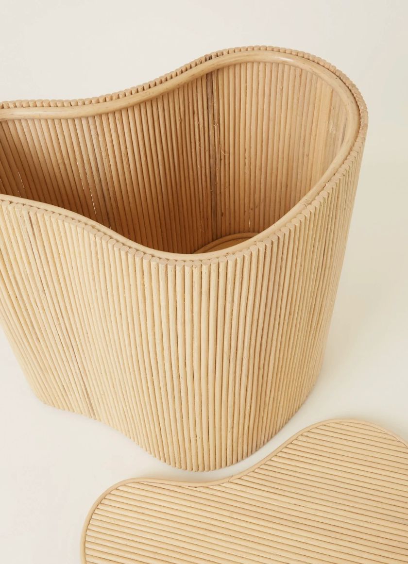 Natural rattan wavy-shaped basket with its lid resting in front, detail on a warm neutral background