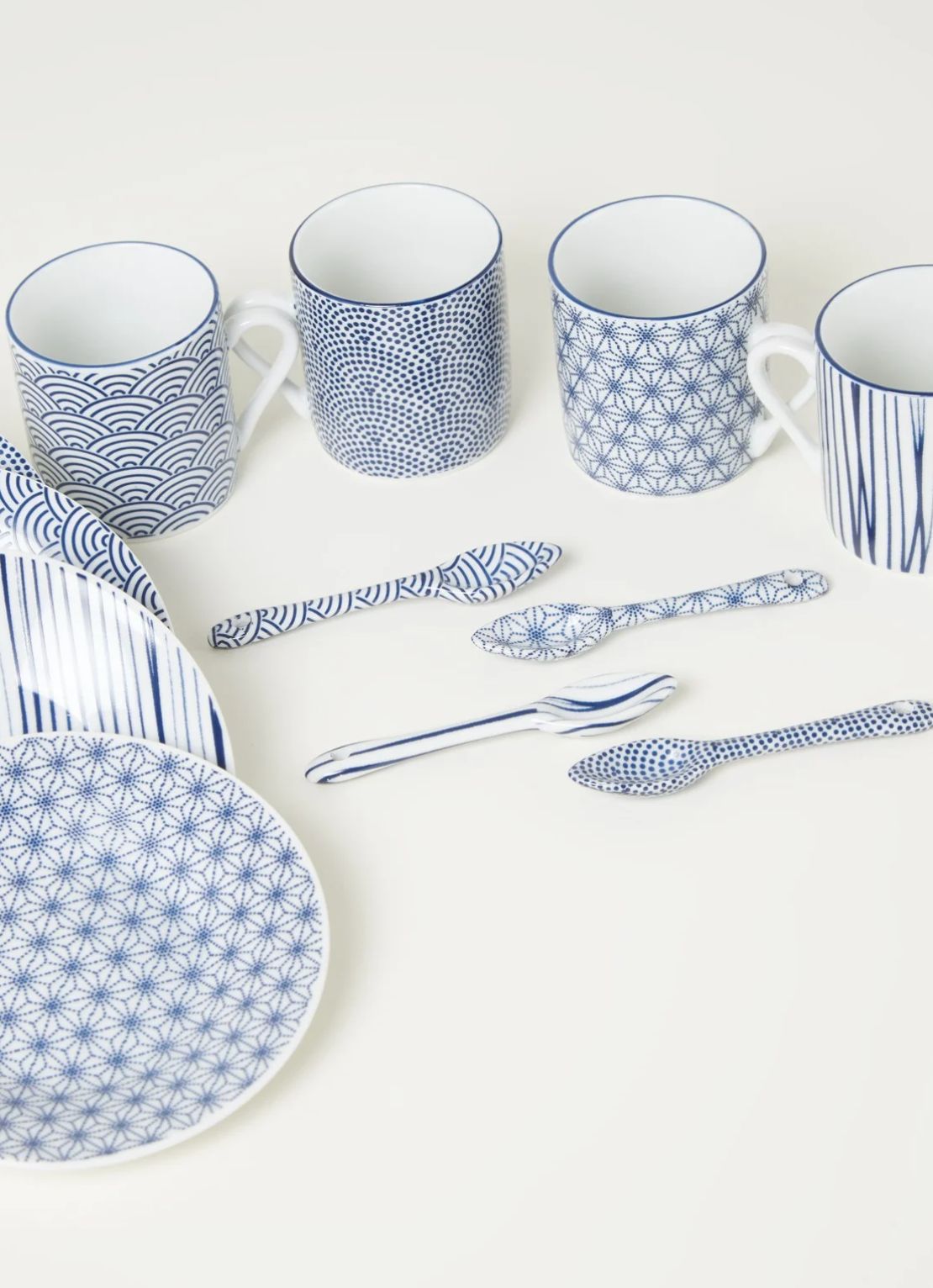 Blue and white Japanese-pattern porcelain mugs, plates and spoons arranged on an off-white surface