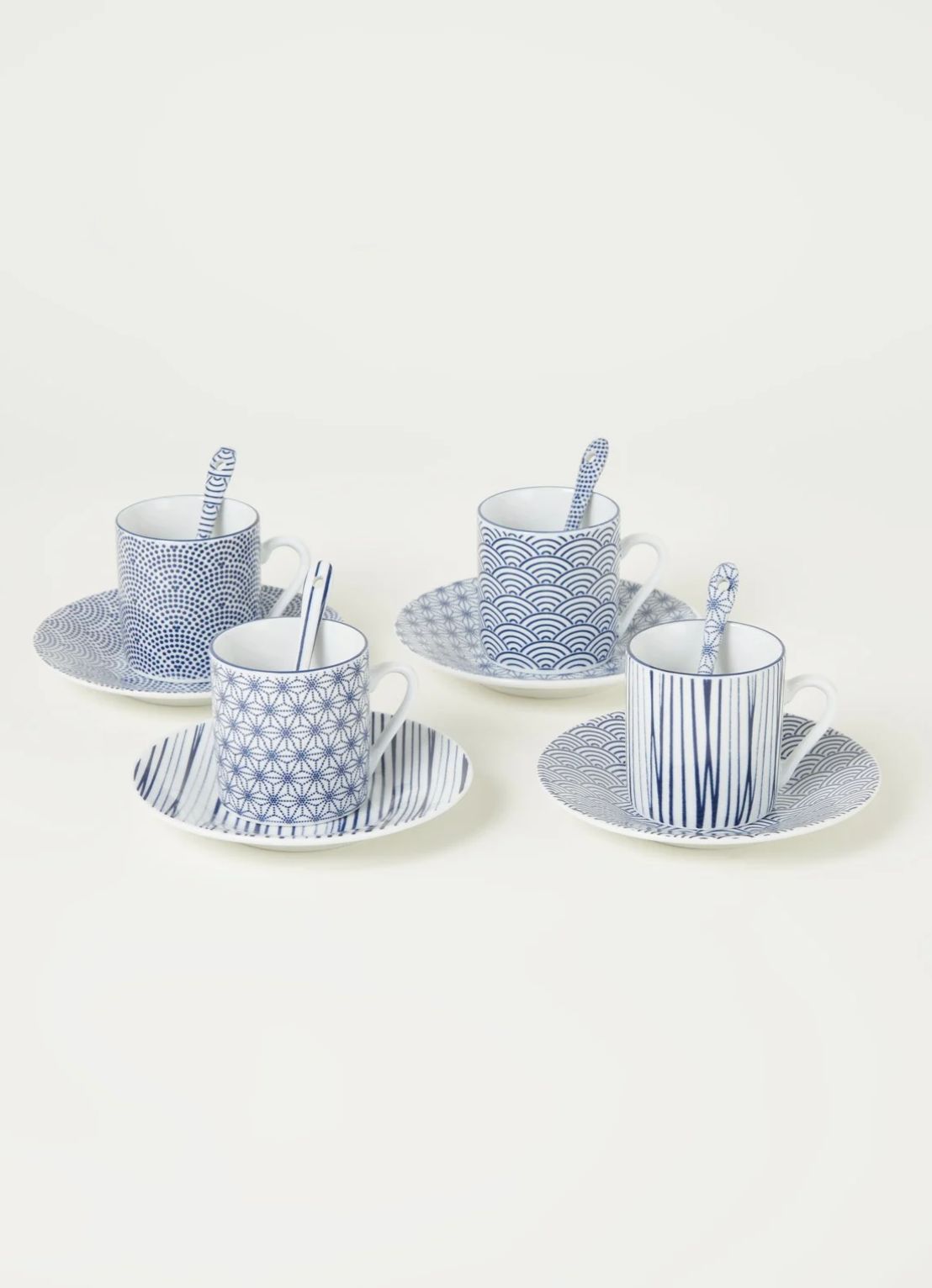 Four blue and white patterned espresso cups with saucers and spoons on a light off-white background