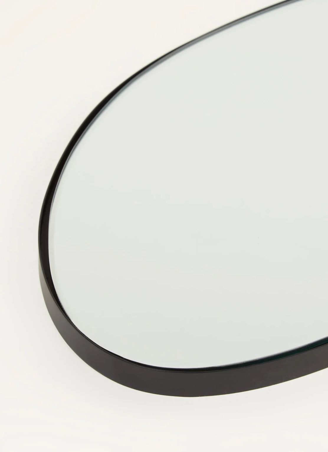 Close-up of an organic-shaped mirror with thin black frame against a pale background