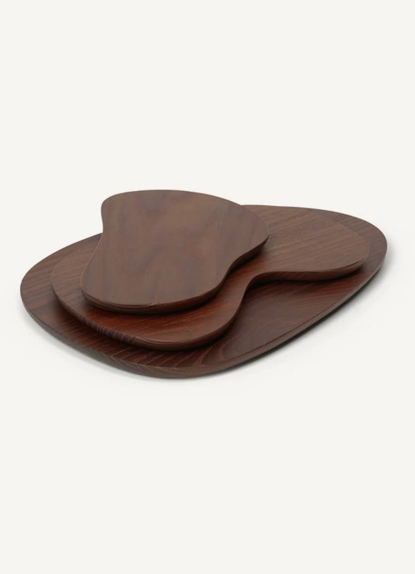 Three dark walnut serving boards of organic shapes stacked on an off-white surface