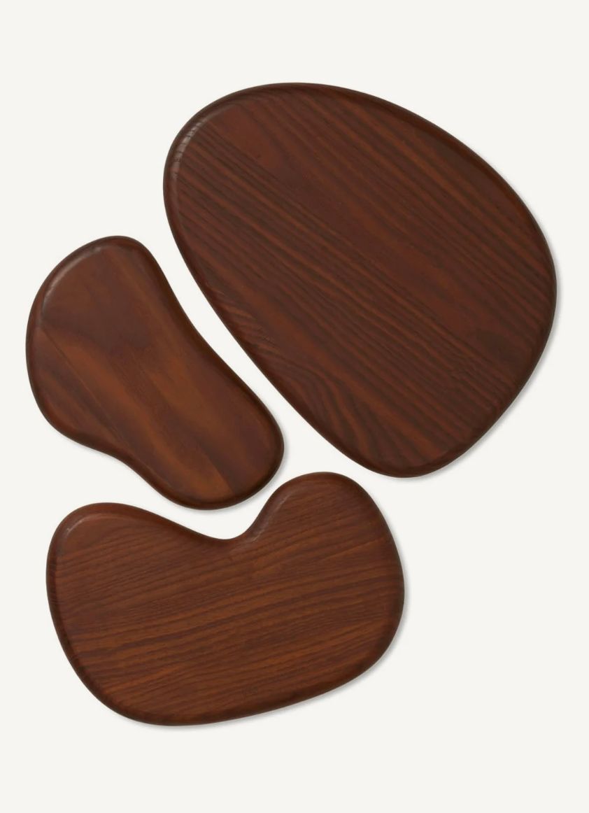 Top view of three dark walnut wooden serving boards of different organic shapes on off-white