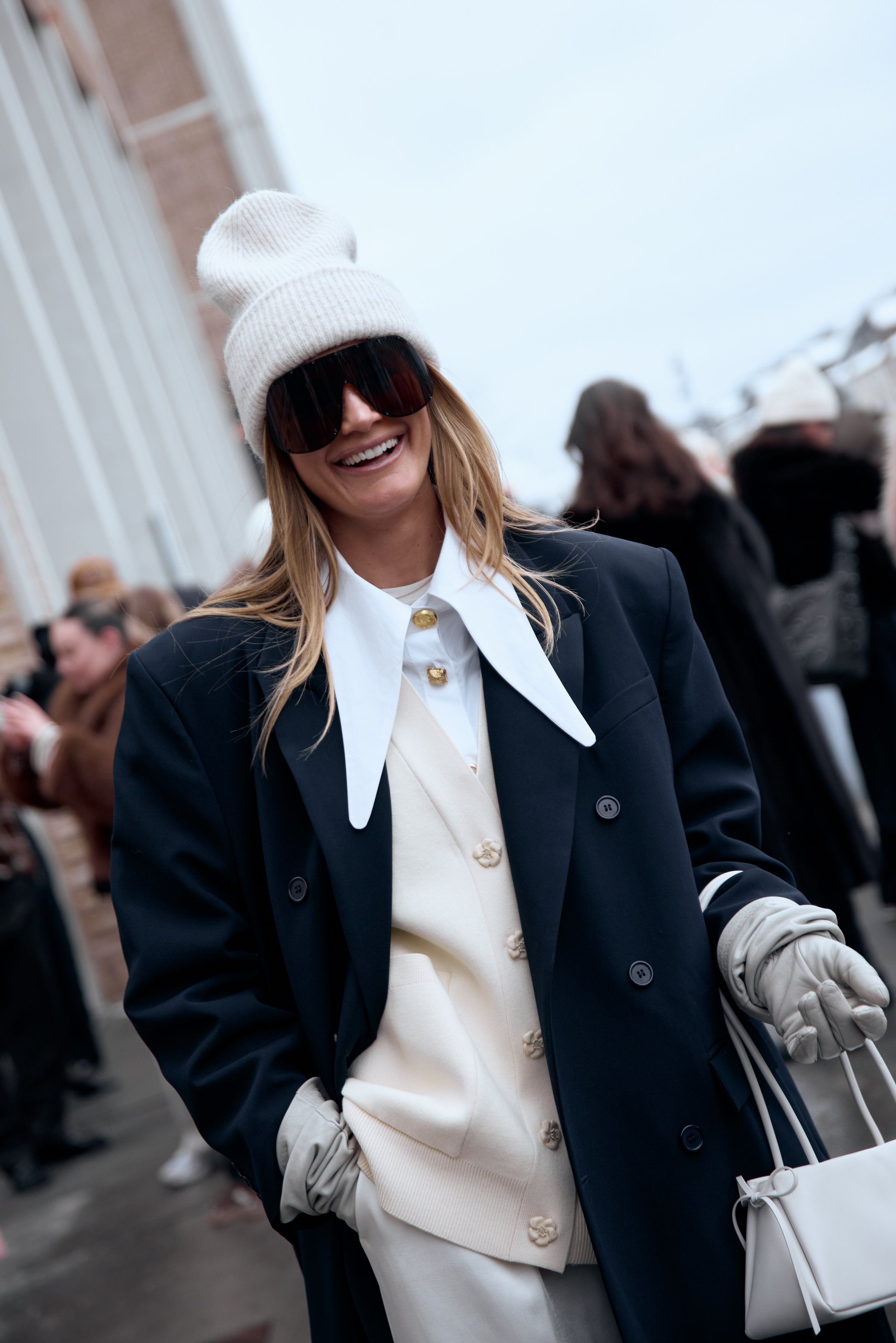 Copenhagen Fashion Week street style: smiling woman in white beanie, navy coat, white collar, cardigan and gloves
