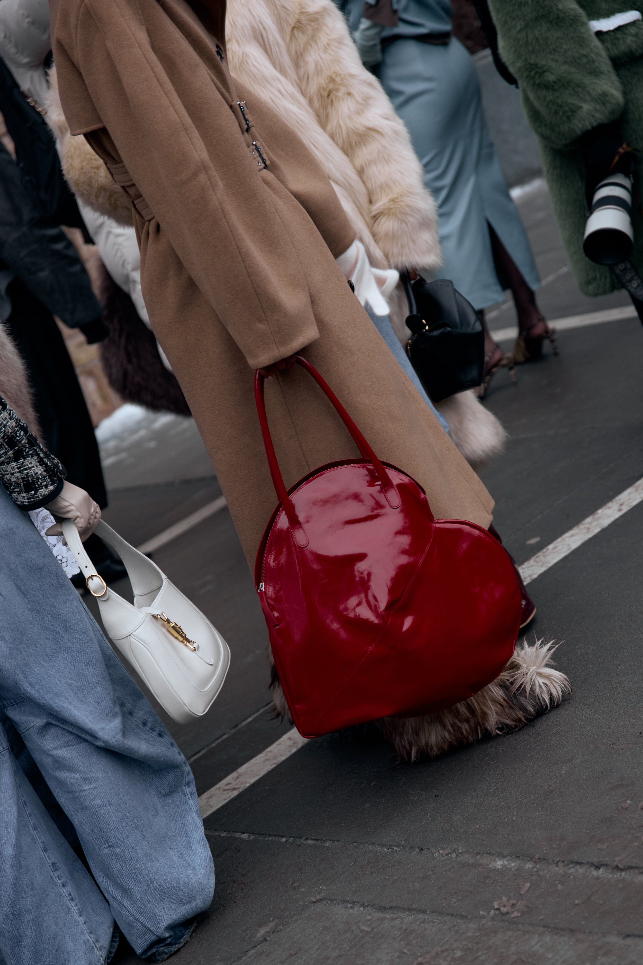 Camel long coat and wide-leg jeans with a glossy red bag, a white shoulder bag held by a passer-by