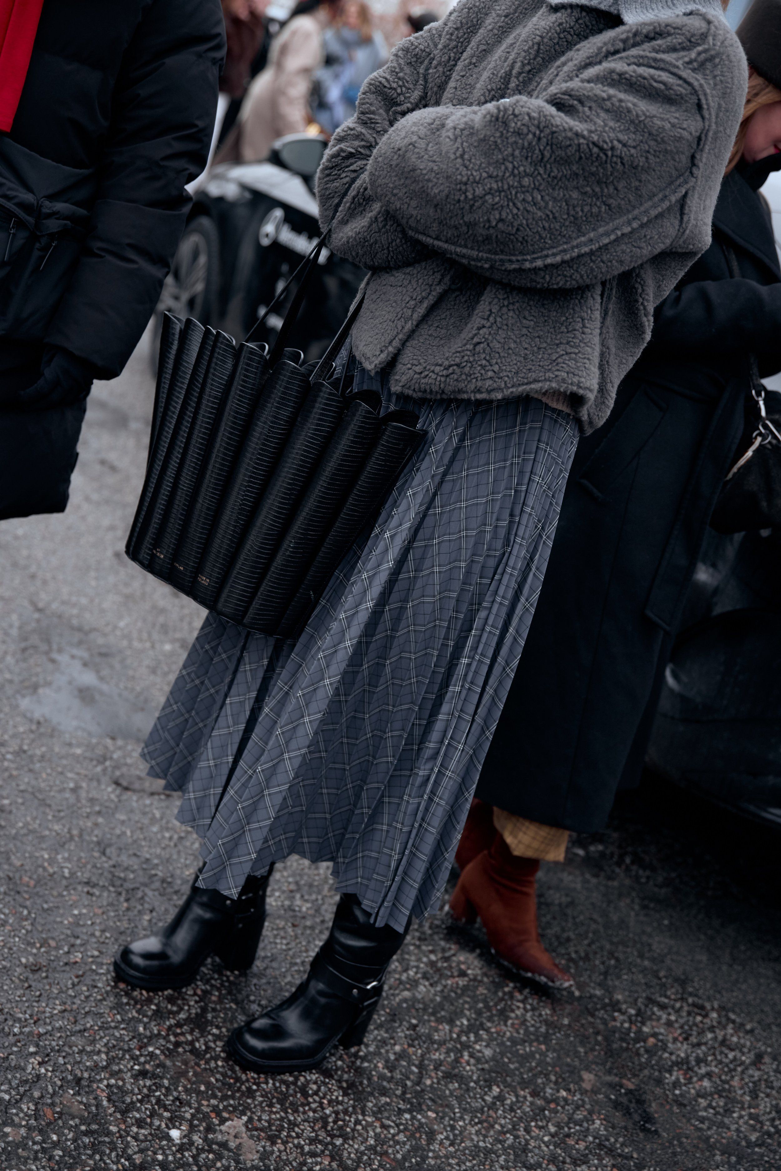 Grey fleece jacket, pleated grey skirt, black quilted tote and chunky black boots on a street