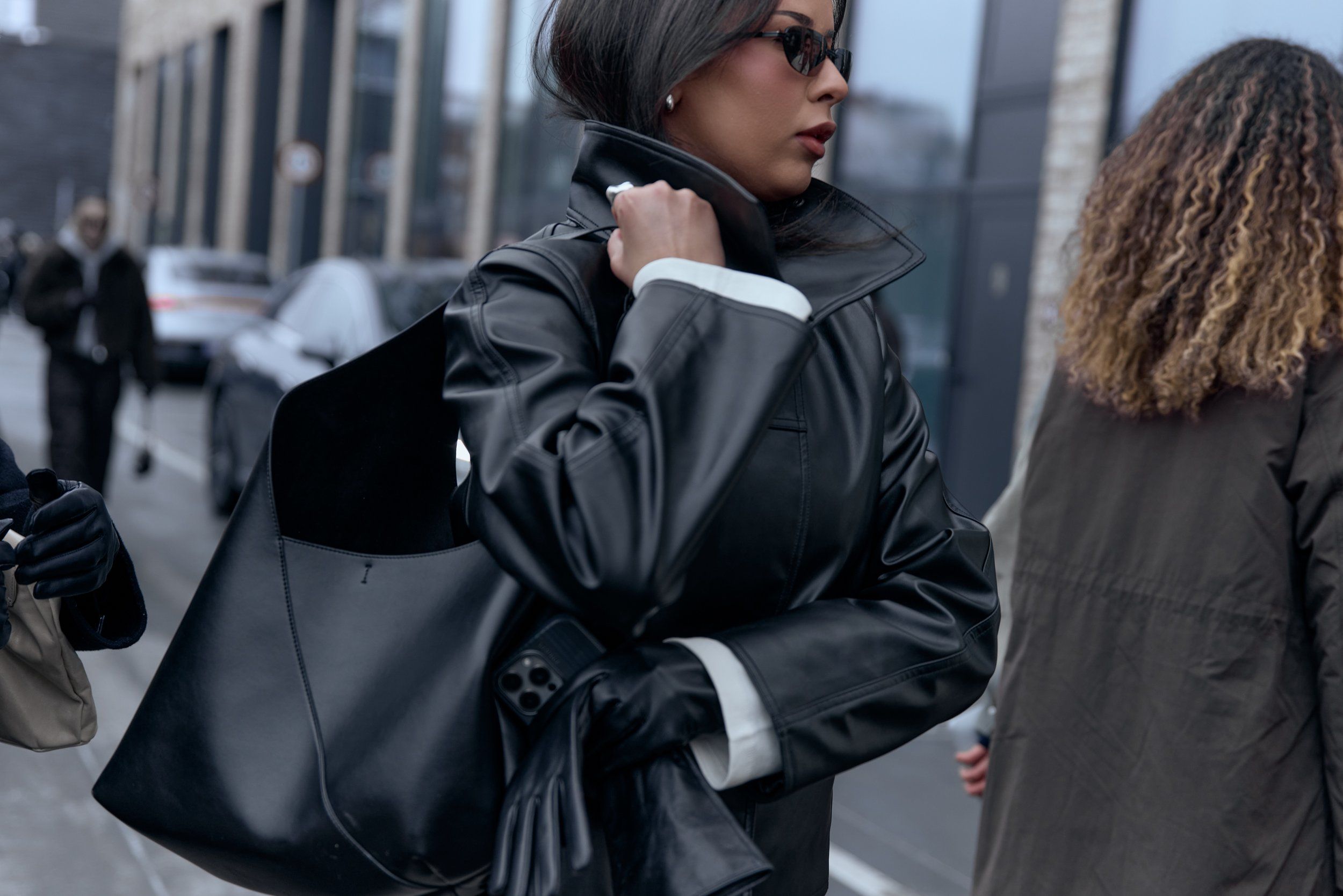 Woman in a black leather coat carrying a large black tote, a second guest in an olive coat behind her