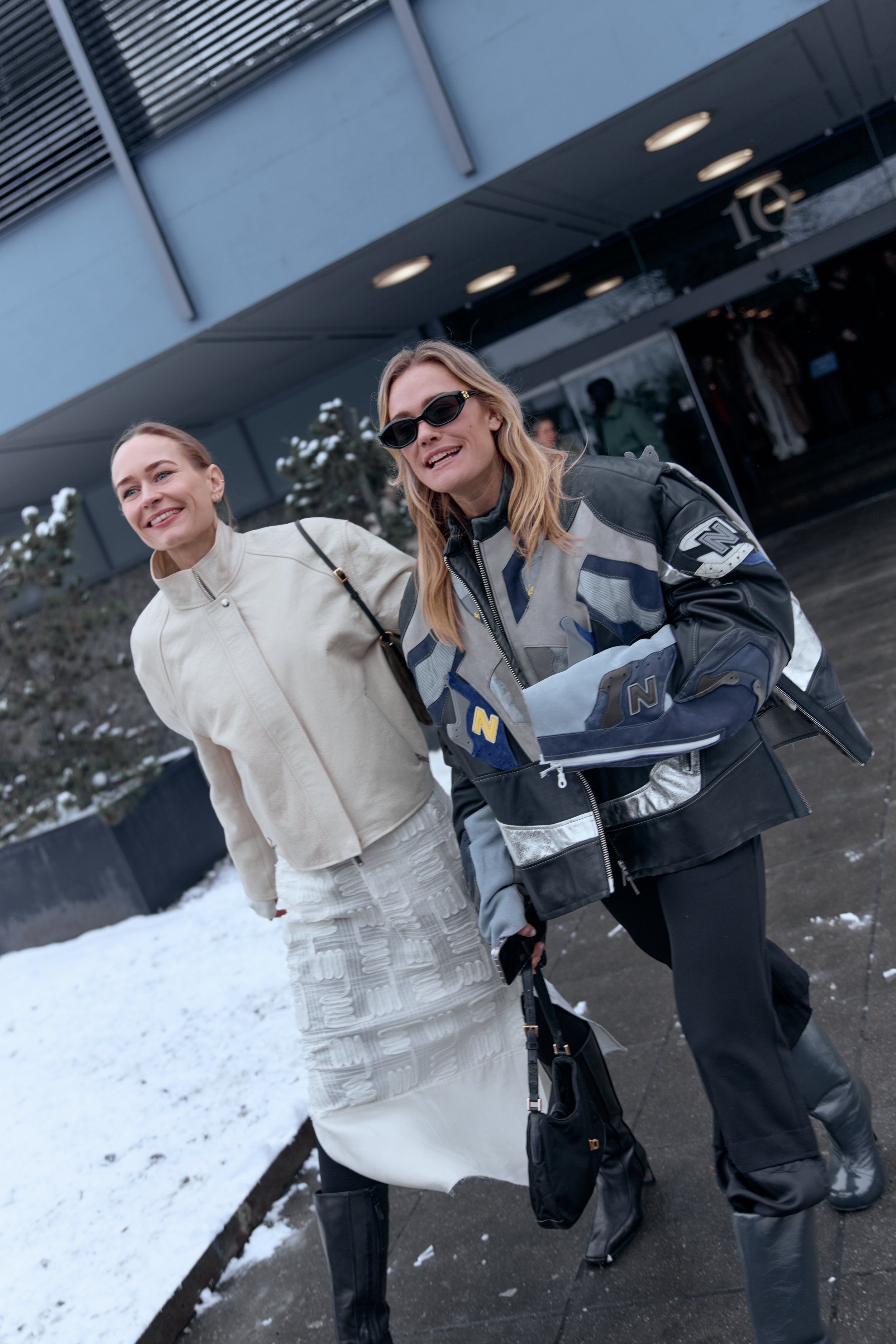 Two smiling guests in the snow, one in a cream jacket and white skirt, one in a panelled racing-style jacket