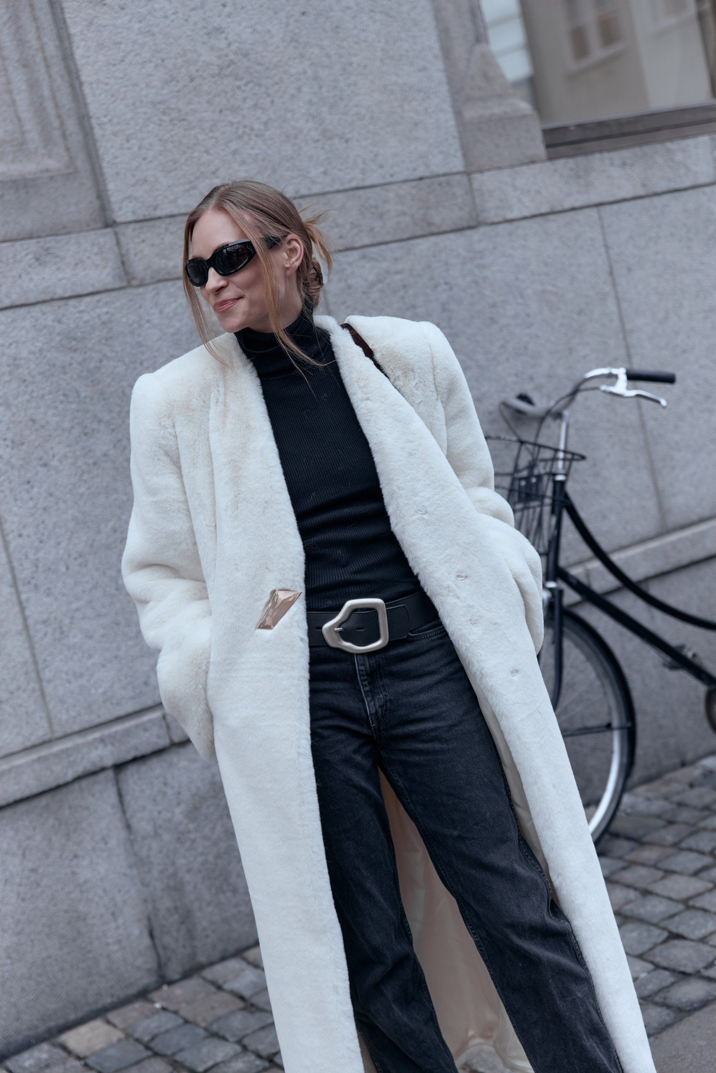Copenhagen Fashion Week street style: long white coat, black polo neck and silver buckle belt by a bicycle