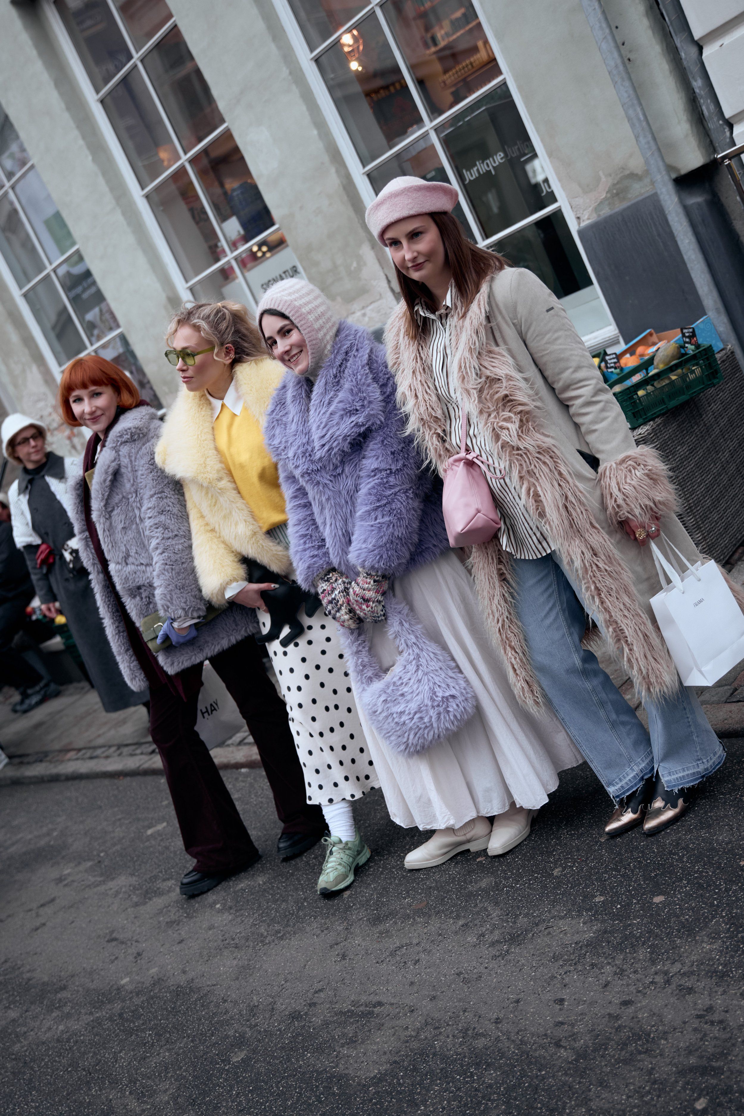Group of four guests in lilac fur, yellow knit and a shaggy beige coat carrying a lilac bag and white tote