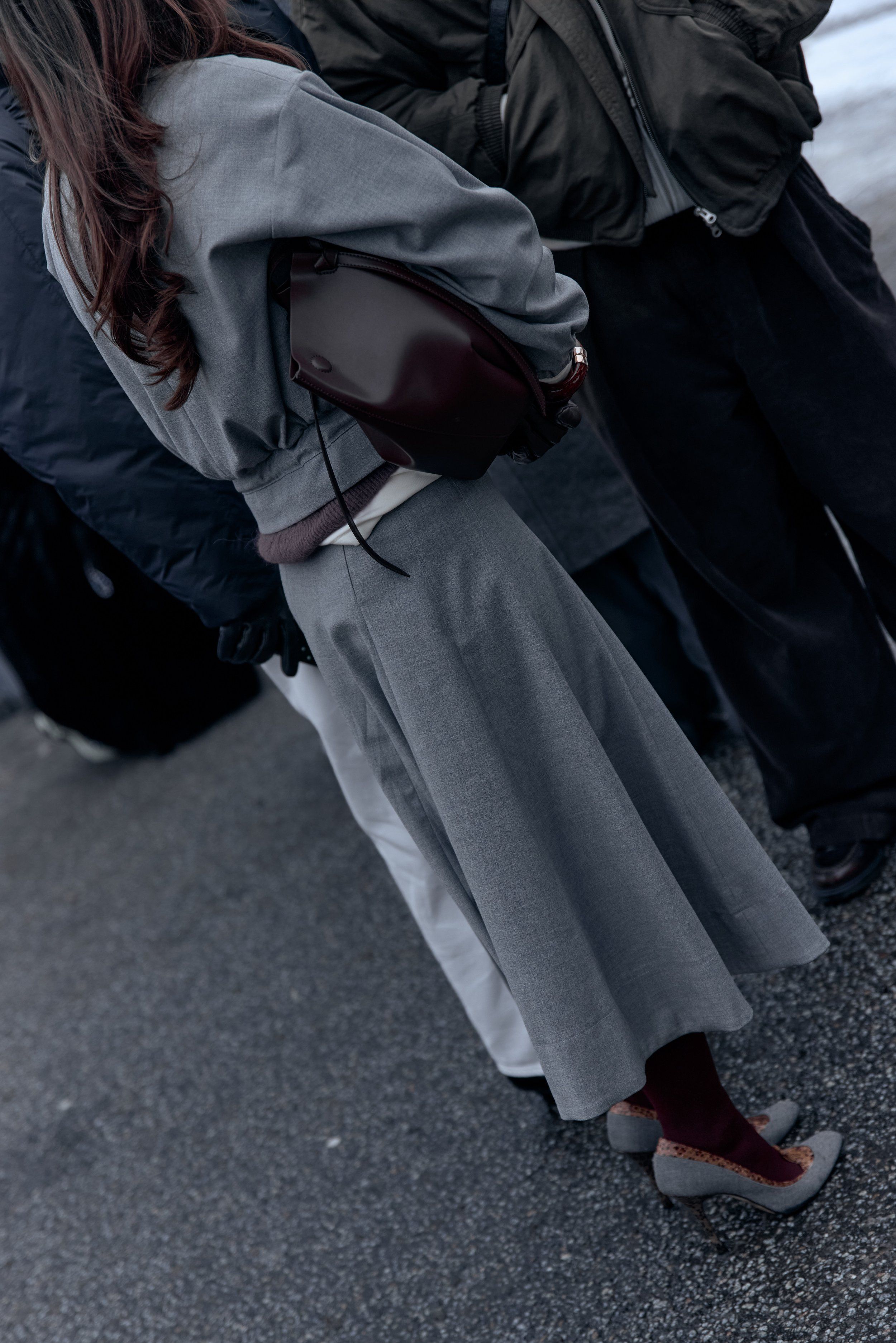 Guest from behind in a grey cropped jacket and long grey skirt with a burgundy shoulder bag