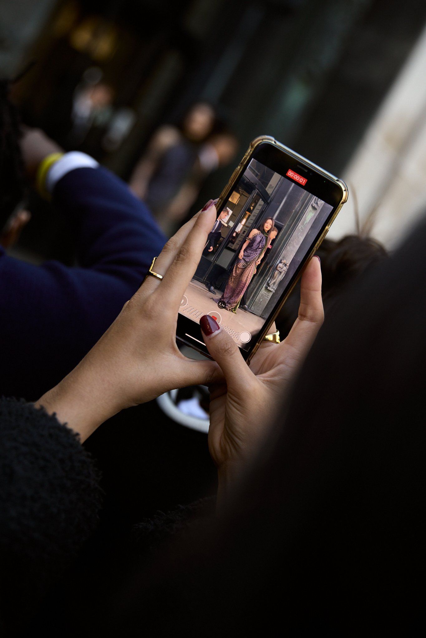 Hands holding a phone photographing a guest on the street, other people blurred behind
