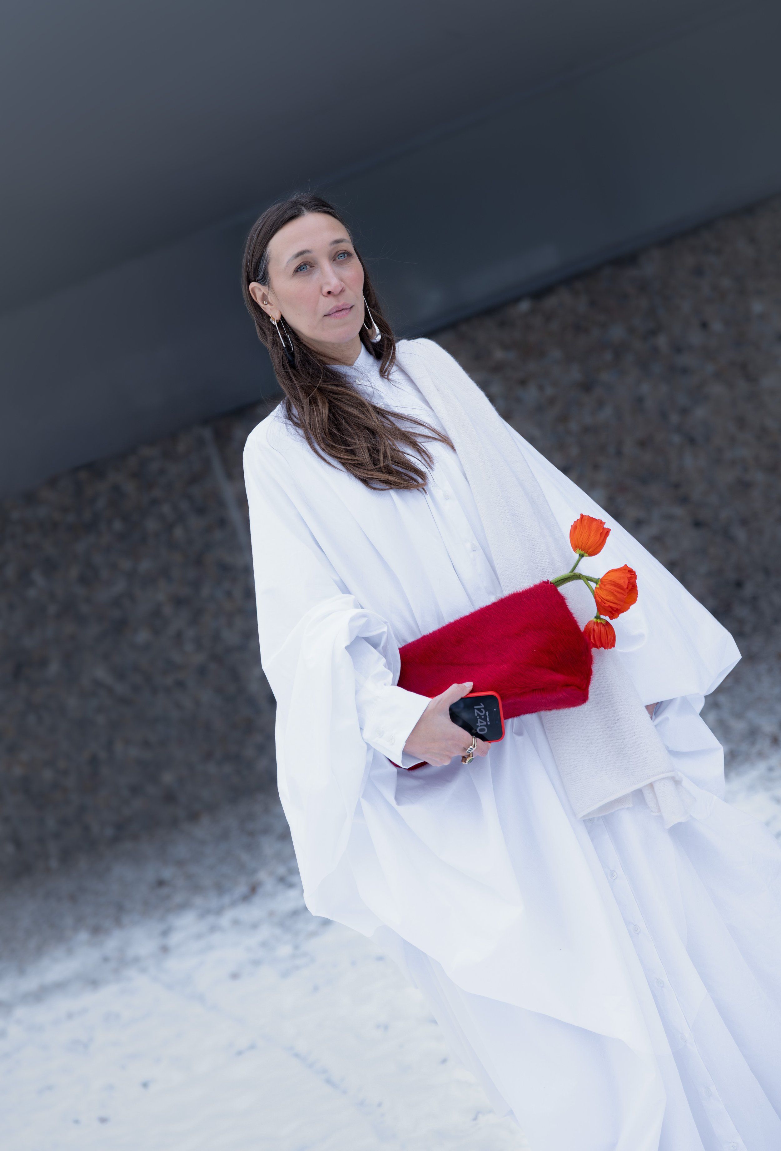 Copenhagen Fashion Week street style: white cape-like shirt dress, red clutch with orange tulips, snow