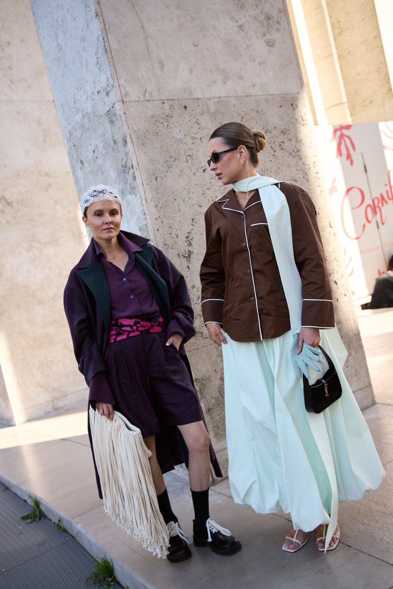 Two guests, one in a purple coat and shorts with a fringed bag, one in a brown jacket and mint skirt