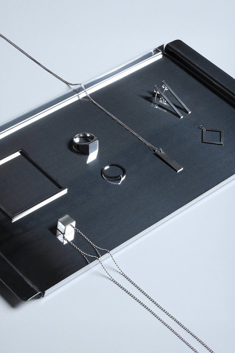 Flat lay of silver jewellery, rings, earrings and chain necklaces on a brushed dark metal tray