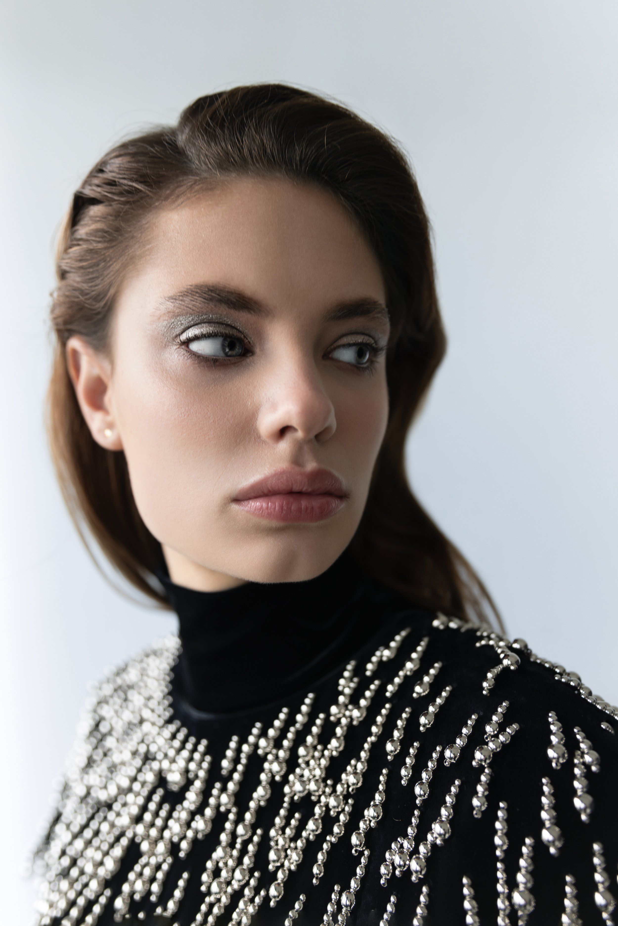Close-up portrait of a model with silver eyeshadow in a black turtleneck with beaded crystal embroidery, grey backdrop