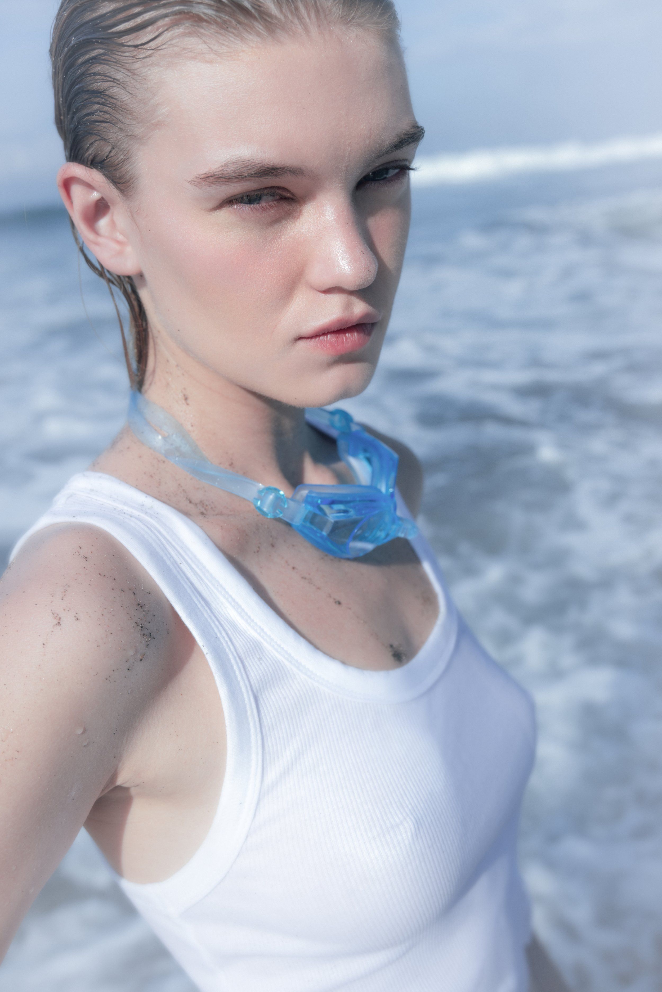 Close-up of a wet-haired model on the beach in a white tank top with a blue translucent collar piece